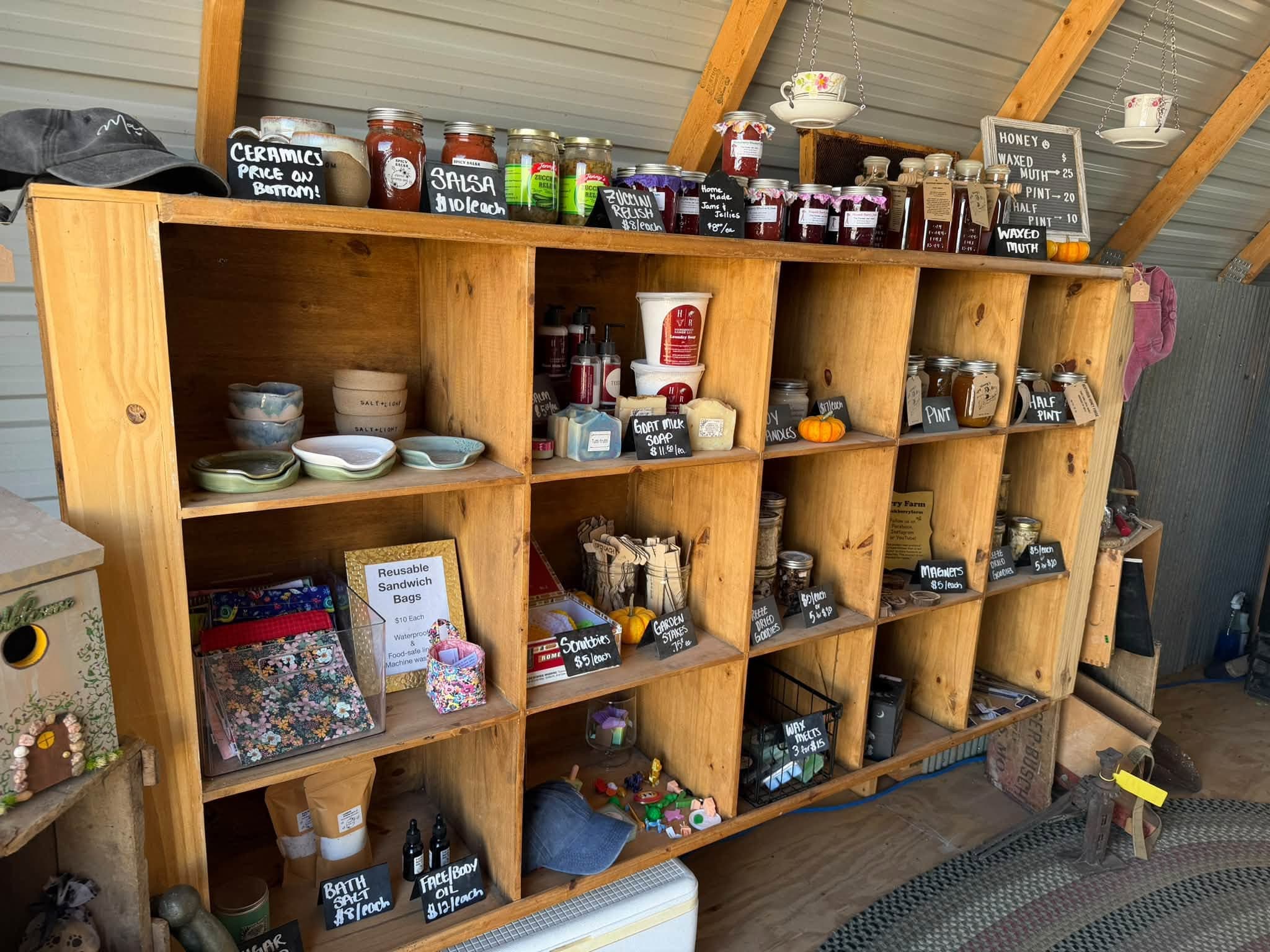 Wooden shelving displaying jarred preserves, ceramics, and farm goods